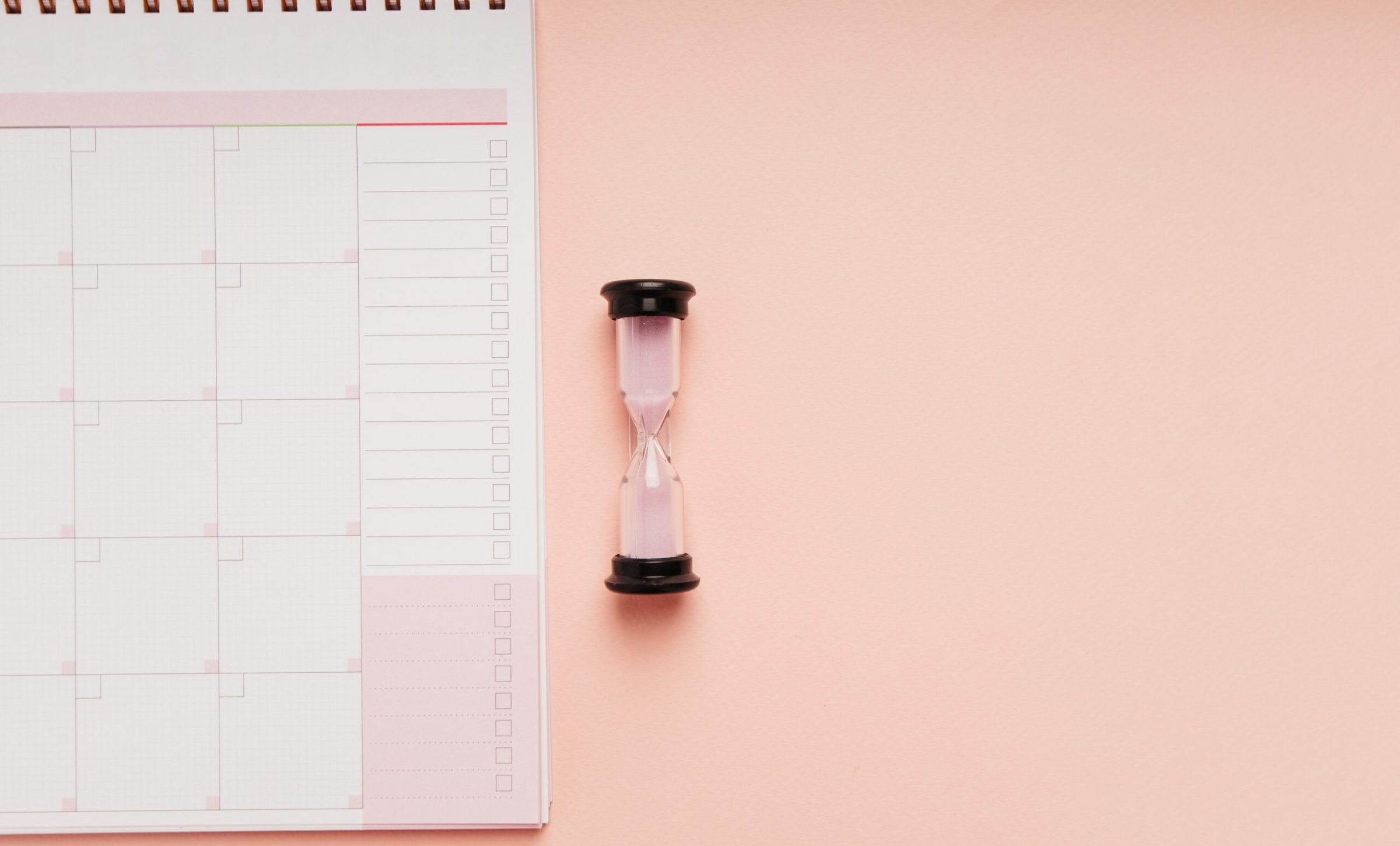 Hourglass with month planner on a pink background, time manageme Hourglass with month planner on a pink background, time management concept.